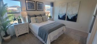 Model Home A bright bedroom in a Medina Crossing home, featuring a plush bed with blue and white accents, framed artwork, and large windows with natural light (Von Ormy, TX).