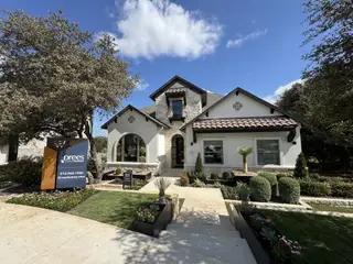 A charming stone-accented home with a tile roof and lush landscaping in Wolf Ranch - 70' by Drees Custom Homes (Georgetown, TX).