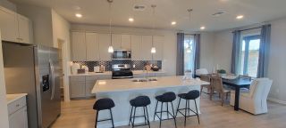 Model Home A modern kitchen with a large island, sleek appliances, and a cozy dining area. Warm lighting creates an inviting atmosphere.