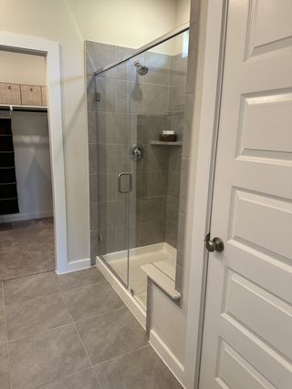 A sleek bathroom featuring a glass-enclosed shower, modern tiling, and an adjacent walk-in closet area.