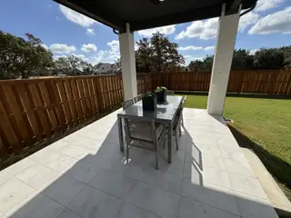 A stylish patio with a glass dining set, tiled flooring, and wooden fencing, perfect for outdoor gatherings.