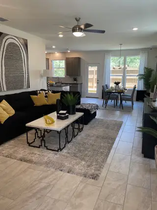 A stylish, open-concept living and dining area in a Villas at Presidio home, featuring a modern black sofa with yellow accents, a dining set, and large windows (San Antonio, TX).