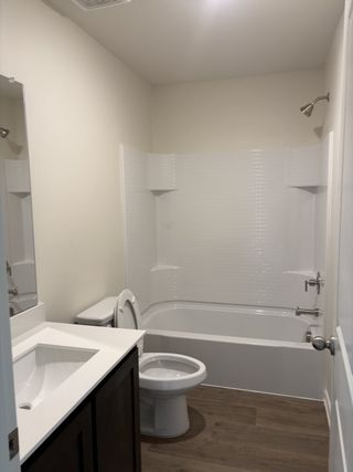 A sleek bathroom with a white-tiled shower, dark vanity, and wood-style flooring.
