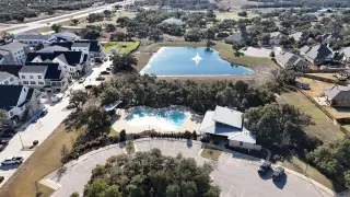 Community Amenities A peaceful aerial view of the Palmera Ridge community by Highland Homes, showcasing homes, a pool, and green spaces in Leander, TX.