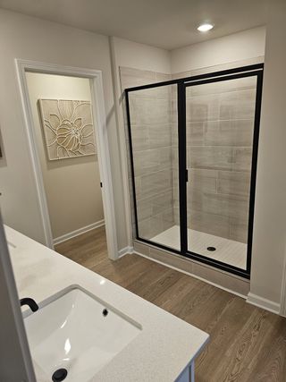 A modern bathroom featuring a sleek glass shower, wood floors, and an elegant wall art piece.