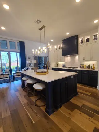 A chic kitchen features a large island, elegant lighting, and sleek cabinetry with a blend of navy and white tones.