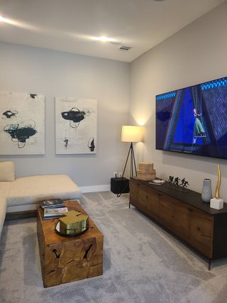 A cozy living room with modern art, a sleek TV setup, and a natural wood coffee table, complemented by plush carpet flooring.