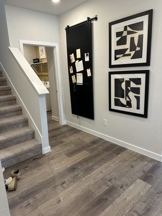 Model Home A modern hallway with sleek wood flooring, abstract art, plush carpeted stairs, and a black sliding barn door.