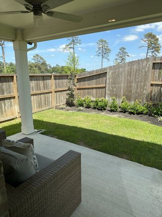 Model Home A cozy covered patio with wicker furniture, lush grass, and a wooden fence offering privacy in a serene outdoor space.