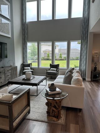 Model Home A spacious living room with lofty windows, modern furnishings, and elegant hardwood floors.