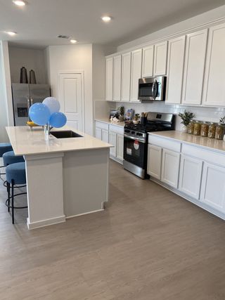A modern kitchen with sleek white cabinets, stainless steel appliances, a central island, and elegant light wood flooring.