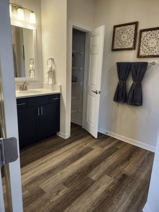 Model Home A modern bathroom with wood-like flooring, sleek vanity, large mirror, open closet, and decorative wall art.
