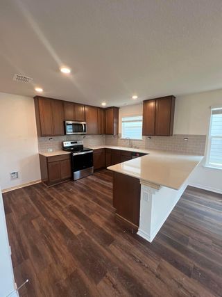 A modern kitchen with dark wood cabinetry, stainless steel appliances, a light quartz countertop island, and warm wood laminate flooring.