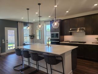 A modern kitchen featuring a sleek island, pendant lights, dark cabinetry, and stainless steel appliances.
