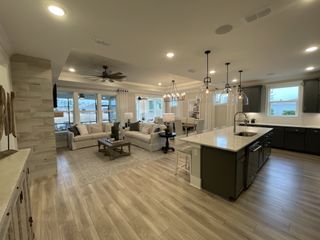A spacious open-plan living area with sleek wood flooring, cozy seating, and a chic kitchen featuring elegant pendant lighting.