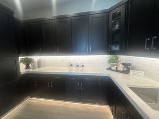 A sleek kitchen with dark cabinetry, white countertops, subway tile backsplash, and under-cabinet lighting.