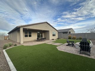 A well-landscaped backyard with artificial turf, a paved walkway, and a covered patio.
