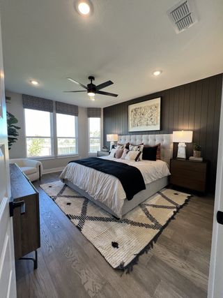 Model Home A cozy bedroom with a tufted headboard, dark accent wall, and plush rug, featuring natural light and warm wood flooring.