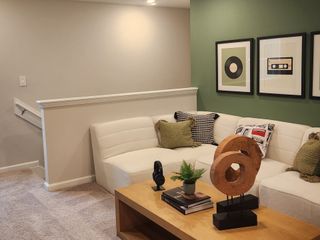 A cozy living room with a cream sectional, green accent wall, and stylish framed artwork, complemented by modern decor.