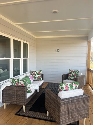A cozy porch with wicker seating, floral cushions, and natural wood flooring, perfect for relaxation and entertaining.