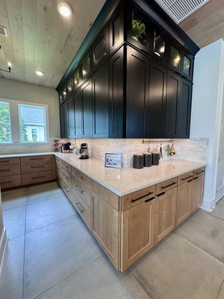 A modern kitchen with black upper cabinets, wooden lower cabinets, light countertops, and ample natural light.