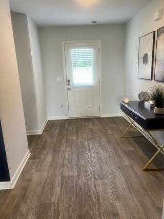 A welcoming entryway with sleek wood floors, modern decor, and a bright painted door featuring natural light.