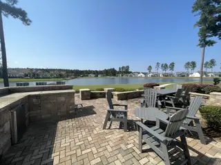 Community Amenities A scenic patio with Adirondack chairs overlooking a tranquil lake in Four Seasons at Lakes of Cane Bay by K. Hovnanian® Homes (Summerville, SC).