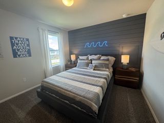 A cozy bedroom with striped bedding, dark accent wall, neon wave light, and soft lighting creates a serene atmosphere.