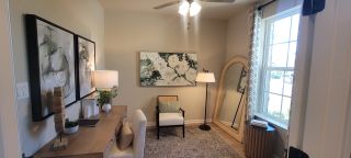 A cozy office space with elegant artwork, wooden desk, stylish chair, floor lamp, and large window for natural light.