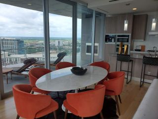 Model Home A modern dining area with a sleek oval table, bold orange chairs, and floor-to-ceiling windows overlooking the city skyline.