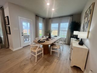 Model Home A cozy dining space with a wooden table, elegant chairs, and soft lighting from modern lamps, opens to a backyard view.