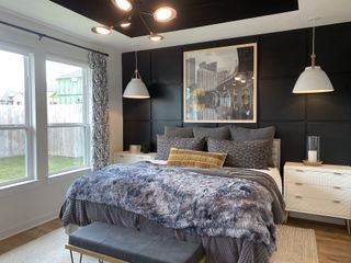 Model Home A cozy bedroom featuring a plush bed, modern pendant lights, and a stylish black accent wall with cityscape artwork.