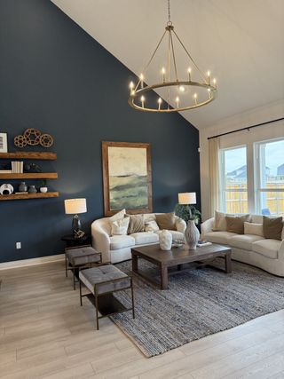 Model Home A cozy living room with a vaulted ceiling, navy accent wall, elegant chandelier, plush sofas, and rustic wooden decor.