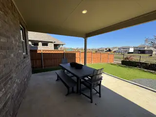 A cozy covered patio with a dining set, overlooking a neatly fenced yard.
