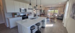 A bright and open-concept kitchen with a large quartz island, modern pendant lighting, and white cabinetry leading into the dining and living space.
