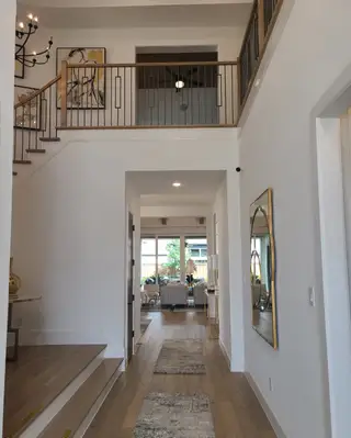 Model Home An elegant foyer with warm wood floors, modern art, and railing, leading to an airy living room with large windows.