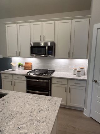 A modern kitchen with sleek granite countertops, white cabinetry, a stainless steel microwave, and stylish lighting.