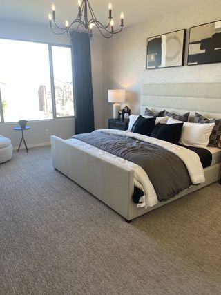Model Home A modern bedroom with textured wallpaper features a tufted headboard, dark accents, and a statement chandelier, offering a stylish retreat.
