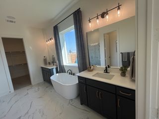 Model Home A stylish bathroom with a marble-tiled bathtub, black vanity, and modern lighting in Solterra Texas by Shaddock Homes (Mesquite, TX).