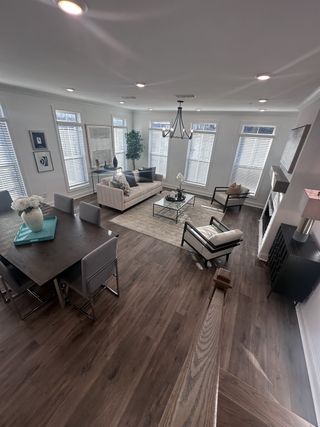 A spacious living area with modern furnishings, dark wood flooring, and ample natural light from large windows.