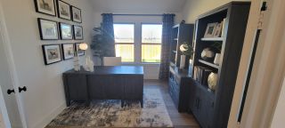 A cozy home office with dark wood furniture, large windows, framed art, and a stylish area rug. Ideal for productivity.