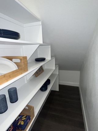 A sleek pantry with white shelving stocked with dishes and essentials, featuring dark wood flooring.
