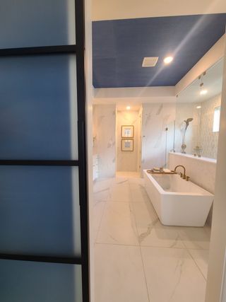 A luxurious bathroom features a sleek freestanding tub, elegant marble floors, and a stylish blue ceiling.