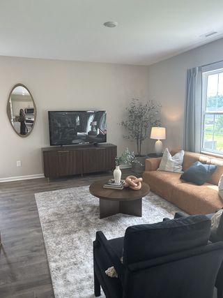 Model Home A cozy living room featuring a brown sofa, sleek TV stand, round coffee table, and elegant decor with natural lighting.