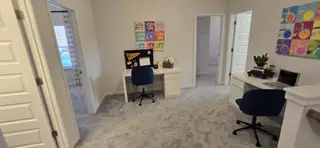 A cozy study area with dual desks, vibrant artwork, and plush carpeting.