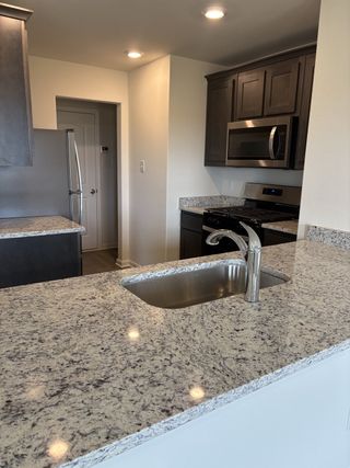 A modern kitchen featuring granite countertops, sleek dark cabinetry, and stainless steel appliances.