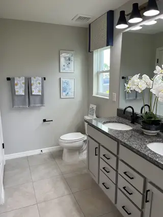 Model Home A modern bathroom featuring a dual-sink granite vanity, elegant lighting, and tasteful wall decor.