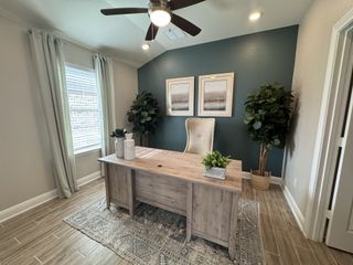 A stylish office featuring a desk, a tufted chair, a bold teal accent wall, and wood-look tile flooring.