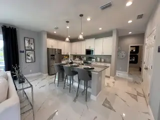 Modern kitchen with sleek white cabinets, marble-tiled floors, a central island, and pendant lighting creating a chic ambiance.