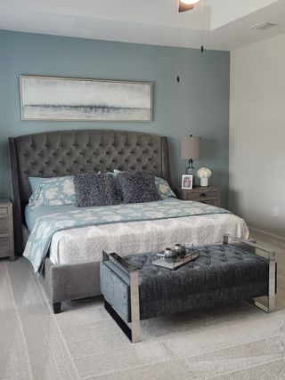 Sophisticated bedroom with a tufted gray bed, elegant bench, and calming blue accent wall.
